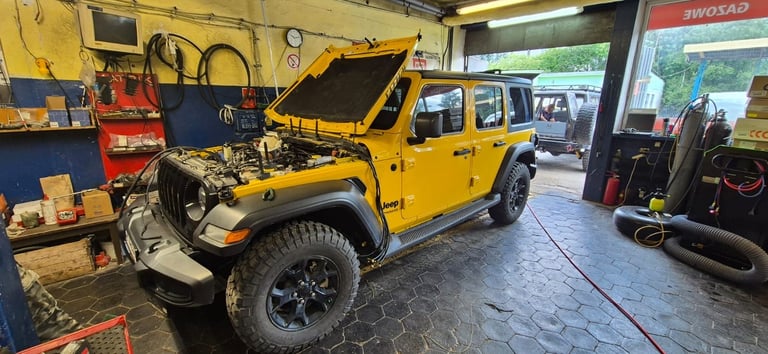 Yellow Jeep Wrangler with open hood in a garage workshop with tools and equipment visible