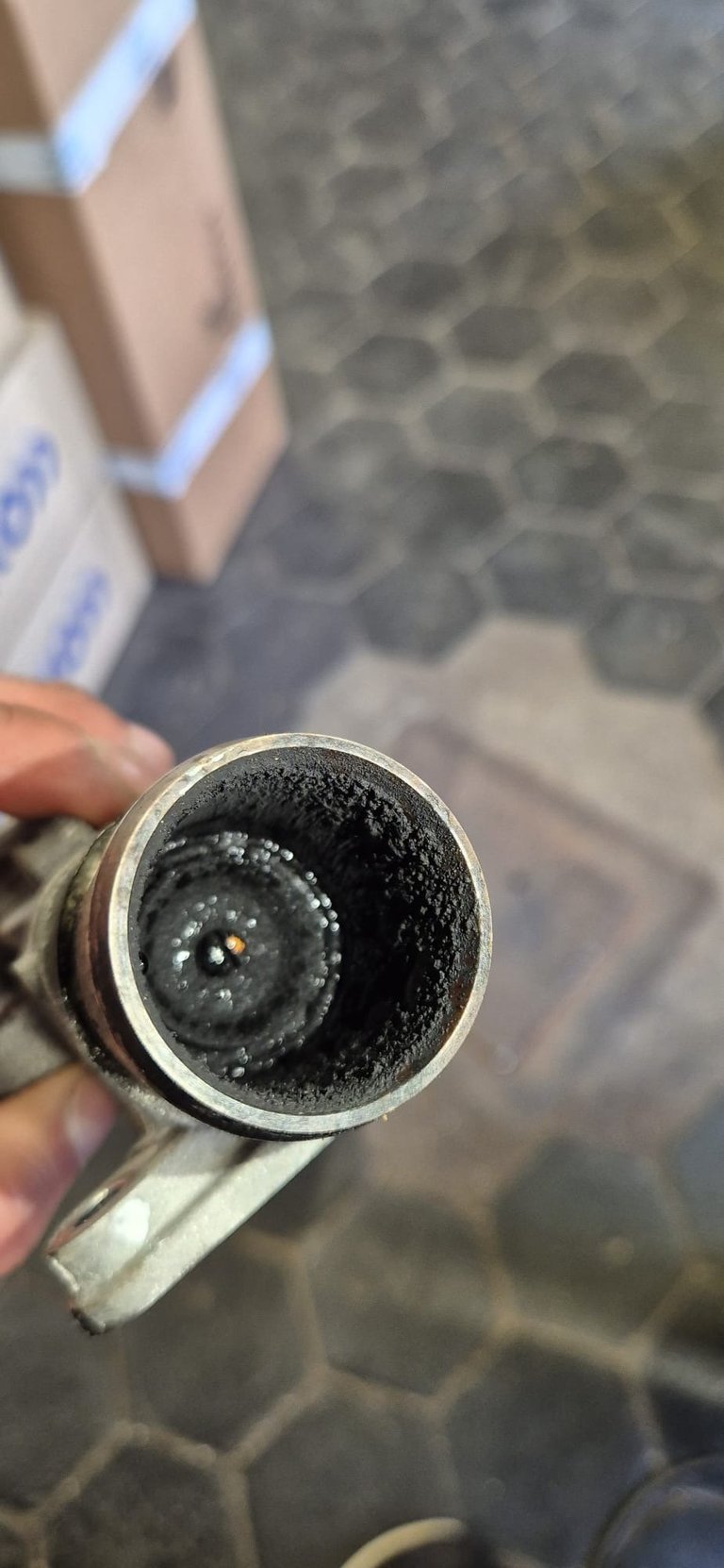 Close-up of a pipe or tube cross-section showing heavy carbon buildup and deposits inside, held by a persons hand